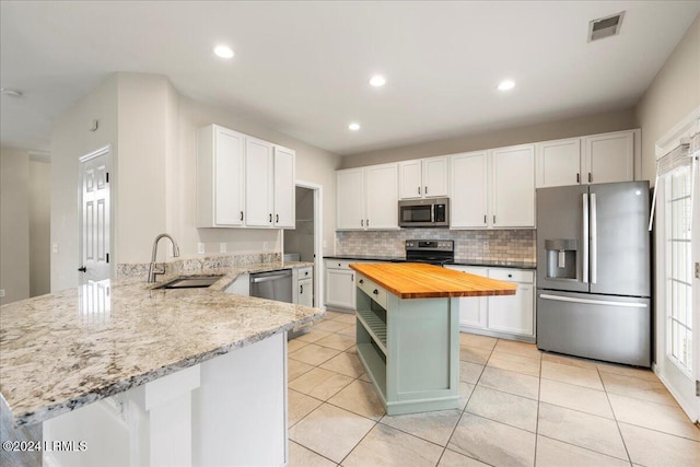 kitchen featuring a kitchen island, white cabinets, wooden counters, kitchen peninsula, and stainless steel appliances