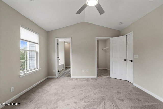 unfurnished bedroom with lofted ceiling, a walk in closet, light colored carpet, ceiling fan, and a closet