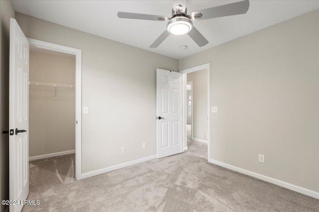 unfurnished bedroom with a walk in closet, light carpet, ceiling fan, and a closet