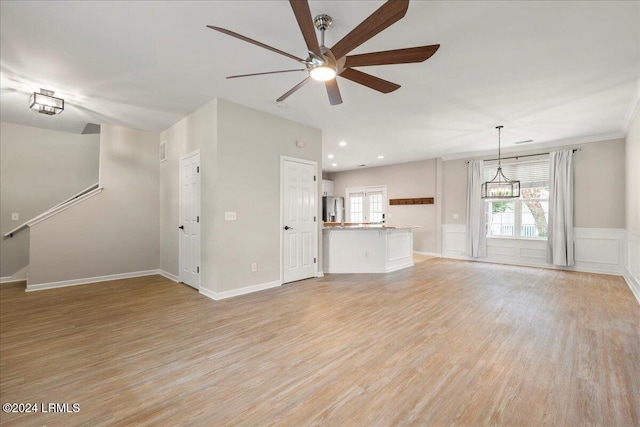 unfurnished living room featuring ceiling fan with notable chandelier and light hardwood / wood-style floors