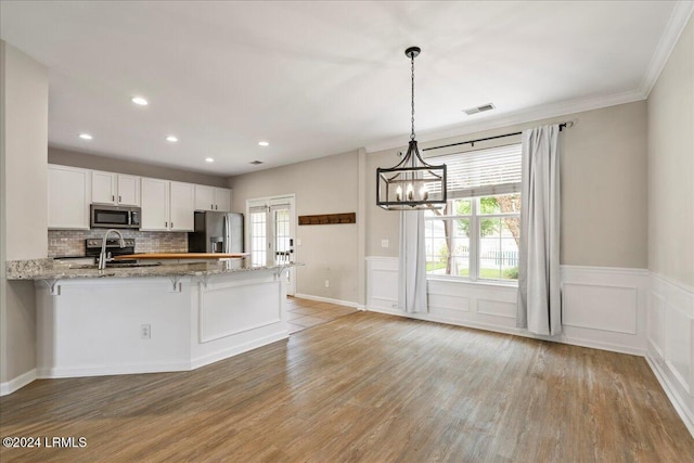 kitchen featuring white cabinetry, light stone counters, hanging light fixtures, kitchen peninsula, and stainless steel appliances