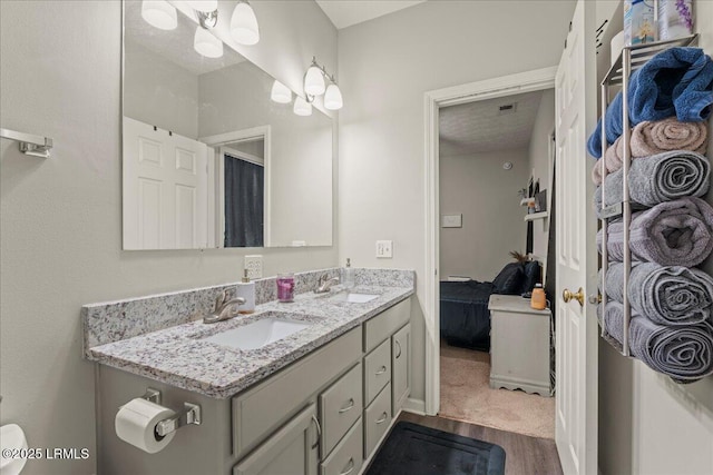 ensuite bathroom with double vanity, a sink, ensuite bath, and wood finished floors