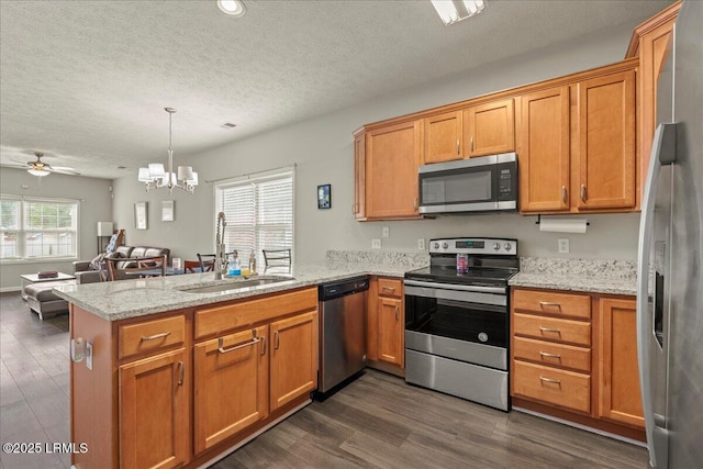 kitchen with stainless steel appliances, ceiling fan with notable chandelier, a sink, dark wood-style floors, and a peninsula