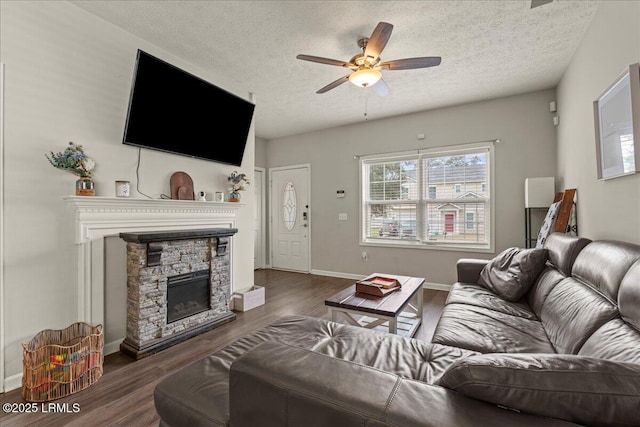 living area featuring a textured ceiling, baseboards, a fireplace, wood finished floors, and a ceiling fan