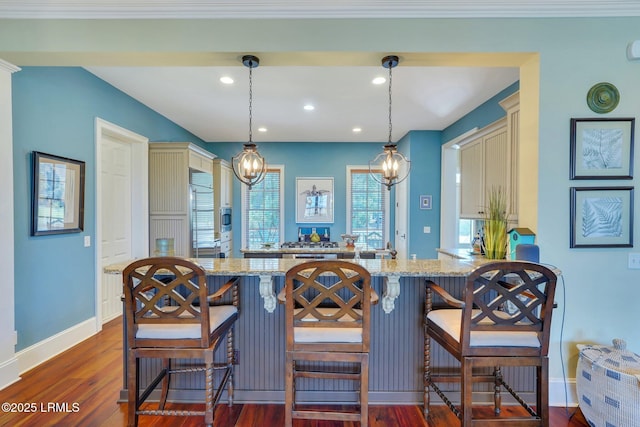 kitchen featuring dark wood-style floors, a breakfast bar area, a peninsula, light stone countertops, and cream cabinets