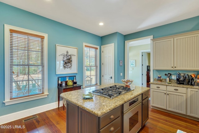 kitchen with visible vents, dark wood finished floors, light stone countertops, cream cabinets, and stainless steel appliances