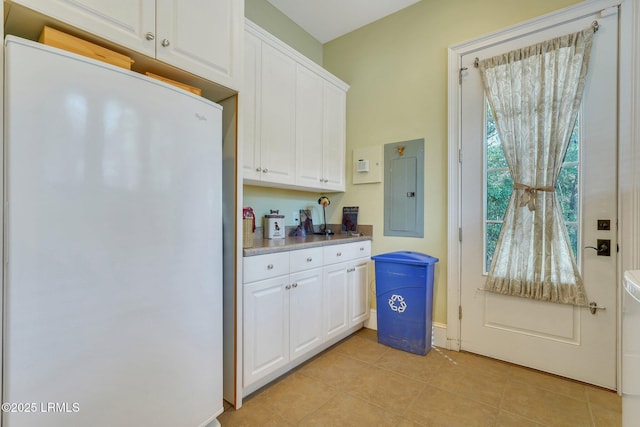 kitchen with light tile patterned floors, electric panel, freestanding refrigerator, light countertops, and white cabinetry