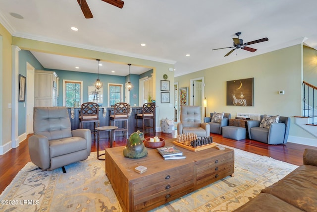 living area with wood finished floors, a ceiling fan, baseboards, ornamental molding, and stairway