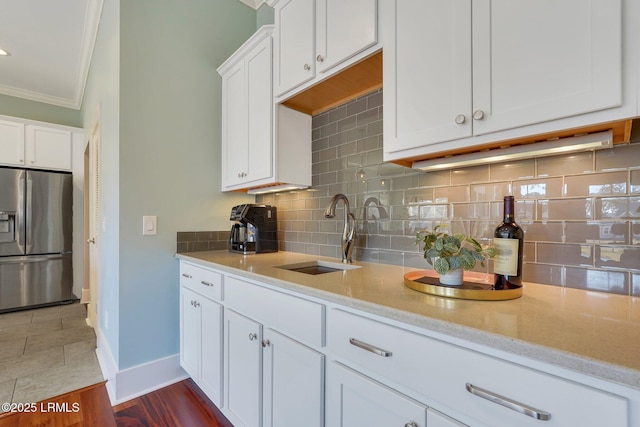 kitchen with a sink, white cabinets, ornamental molding, stainless steel fridge with ice dispenser, and tasteful backsplash