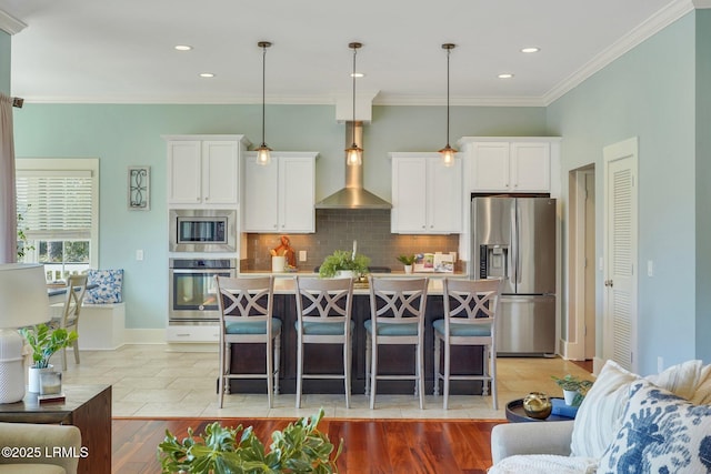 kitchen featuring white cabinets, wall chimney range hood, appliances with stainless steel finishes, and decorative backsplash