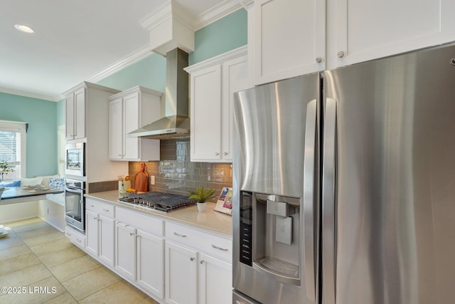 kitchen featuring crown molding, stainless steel appliances, light countertops, backsplash, and wall chimney exhaust hood