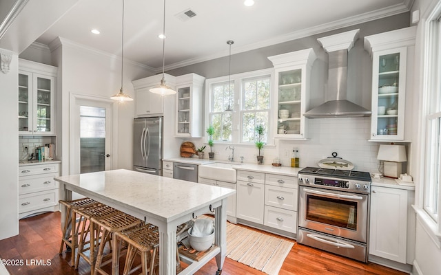 kitchen with white cabinetry, hanging light fixtures, wall chimney exhaust hood, and appliances with stainless steel finishes