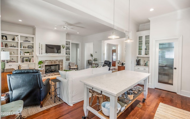 kitchen with a kitchen bar, hanging light fixtures, ornamental molding, a brick fireplace, and dark wood-type flooring