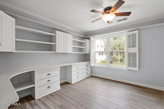 unfurnished office with ornamental molding, built in desk, ceiling fan, and light hardwood / wood-style floors