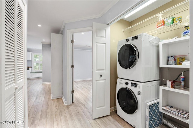 washroom featuring stacked washer / drying machine, crown molding, and light hardwood / wood-style flooring