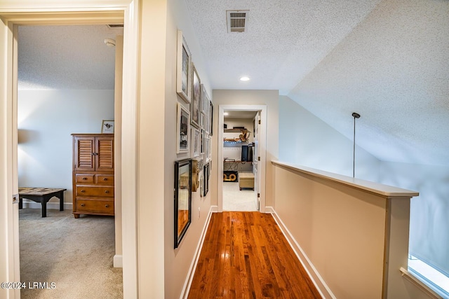 hallway with vaulted ceiling, wood-type flooring, and a textured ceiling