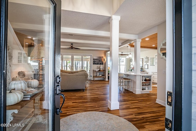 foyer with ornate columns, a textured ceiling, dark hardwood / wood-style floors, ceiling fan, and beam ceiling