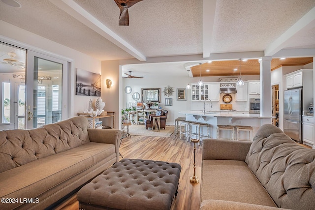 living room featuring ornate columns, beam ceiling, ceiling fan, a textured ceiling, and light hardwood / wood-style flooring