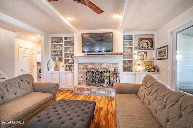 living room featuring built in features, plenty of natural light, a textured ceiling, washer / dryer, and light wood-type flooring