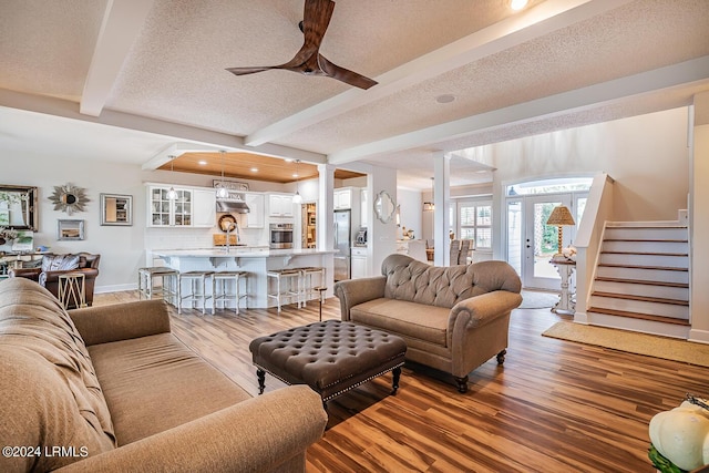 living room with hardwood / wood-style flooring, ceiling fan, decorative columns, a textured ceiling, and beamed ceiling