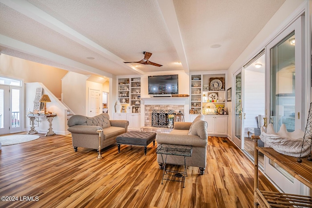 living room featuring built in shelves, light hardwood / wood-style flooring, a textured ceiling, and beamed ceiling