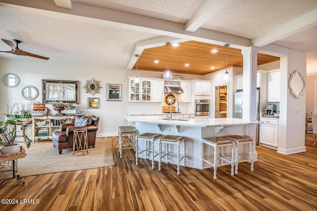 kitchen featuring white cabinetry, stainless steel appliances, tasteful backsplash, an island with sink, and beamed ceiling