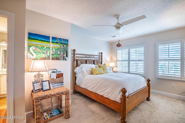 bedroom featuring a textured ceiling, ensuite bath, light colored carpet, and ceiling fan