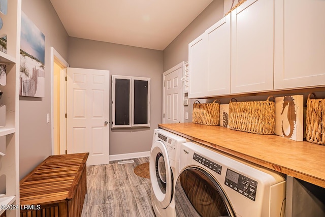 laundry area featuring cabinets, washing machine and dryer, and light hardwood / wood-style flooring