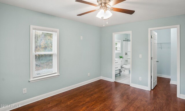 unfurnished bedroom with ensuite bath, dark wood-type flooring, ceiling fan, a spacious closet, and a closet