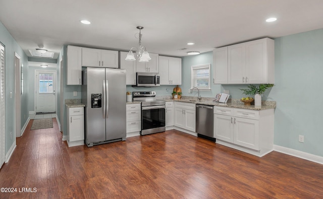 kitchen with dark wood-type flooring, appliances with stainless steel finishes, light stone countertops, white cabinets, and decorative light fixtures