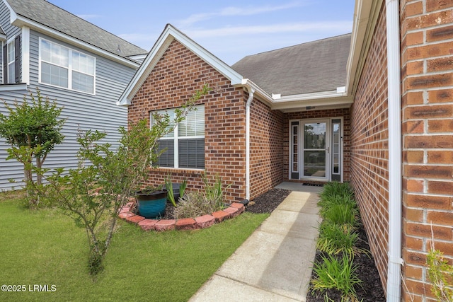 doorway to property with a lawn, brick siding, and a shingled roof