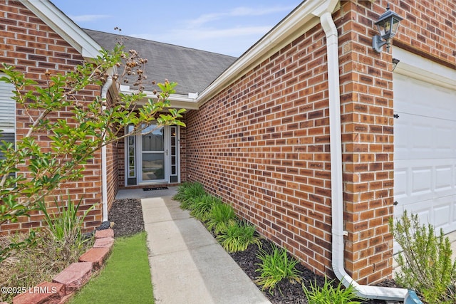 view of exterior entry featuring brick siding, an attached garage, and roof with shingles