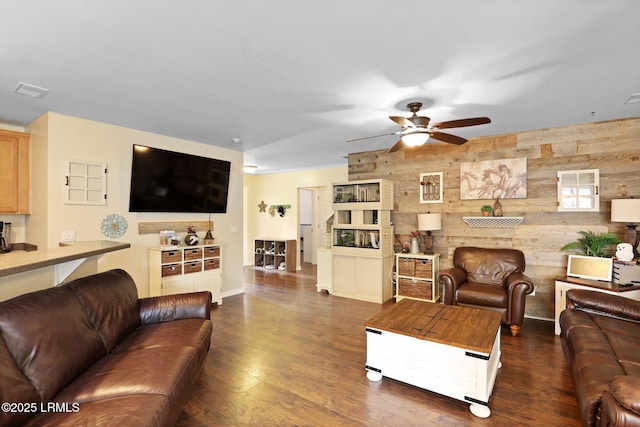 living area featuring a ceiling fan, wood walls, visible vents, and dark wood-type flooring