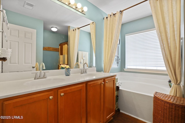 full bathroom with wood finished floors, double vanity, a sink, and tiled tub