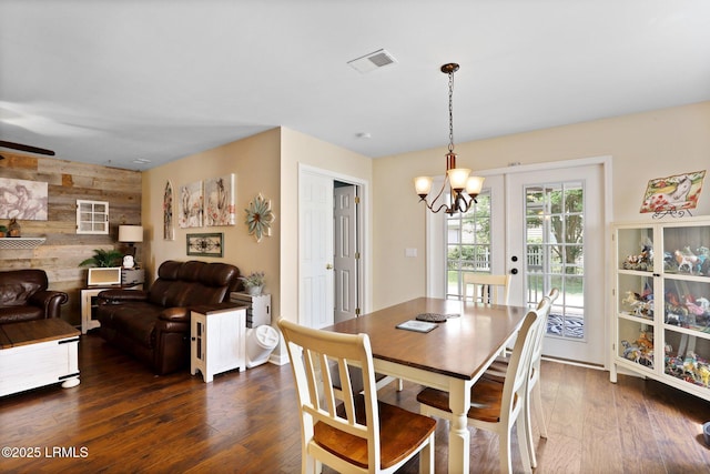 dining room with visible vents, a chandelier, wooden walls, an accent wall, and dark wood-type flooring
