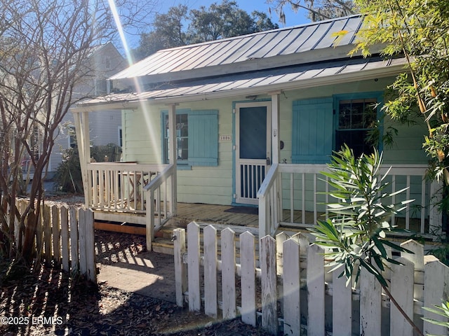 bungalow-style house featuring covered porch, metal roof, a standing seam roof, and fence