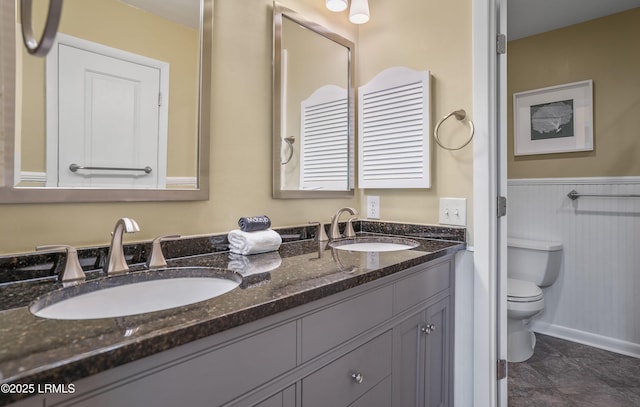 bathroom with wainscoting, a sink, toilet, and double vanity