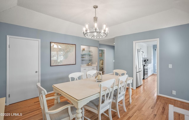 dining room with light wood-type flooring, baseboards, and an inviting chandelier