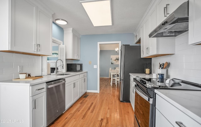 kitchen featuring light wood-style flooring, under cabinet range hood, white cabinetry, light countertops, and appliances with stainless steel finishes