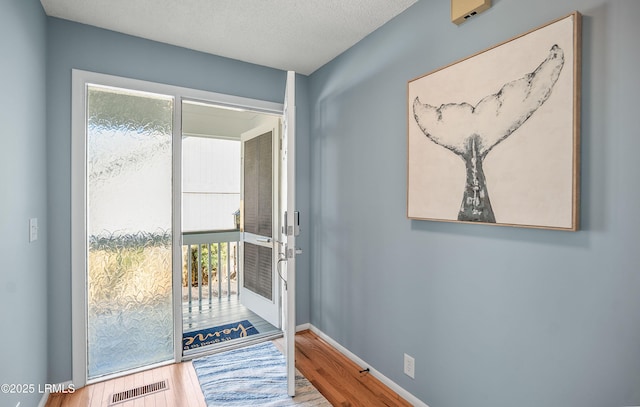 doorway featuring baseboards, a textured ceiling, visible vents, and wood finished floors