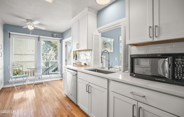 kitchen with black microwave, a sink, white cabinets, stainless steel dishwasher, and light wood finished floors