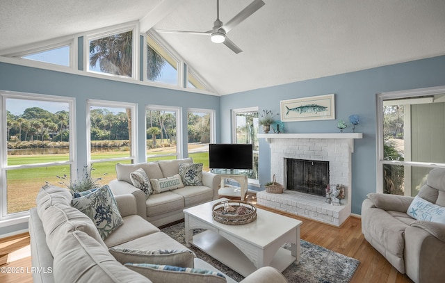 living area featuring a brick fireplace, wood finished floors, a ceiling fan, and a healthy amount of sunlight