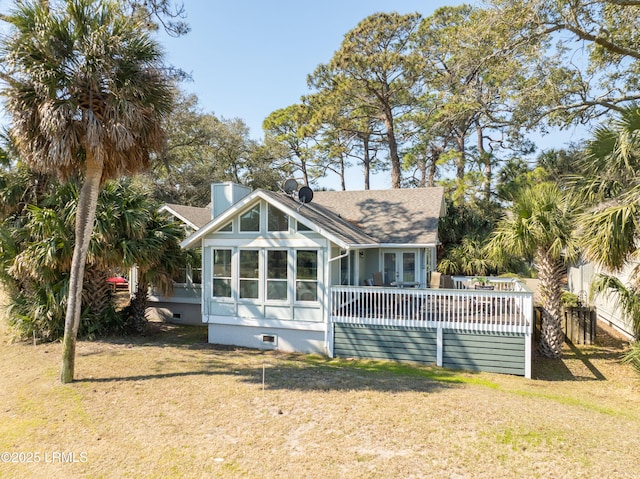 back of property with a chimney, a shingled roof, a lawn, a sunroom, and a wooden deck