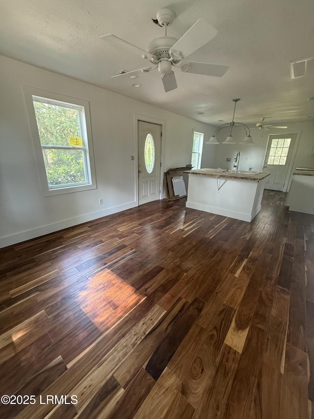 unfurnished living room with dark wood-type flooring, ceiling fan, and plenty of natural light