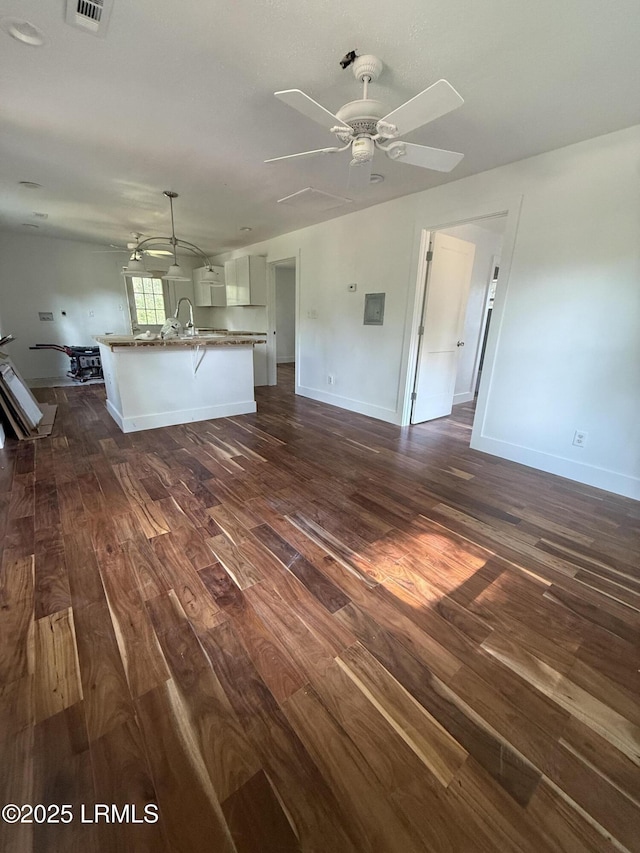 unfurnished living room with dark wood-style flooring, a ceiling fan, and baseboards