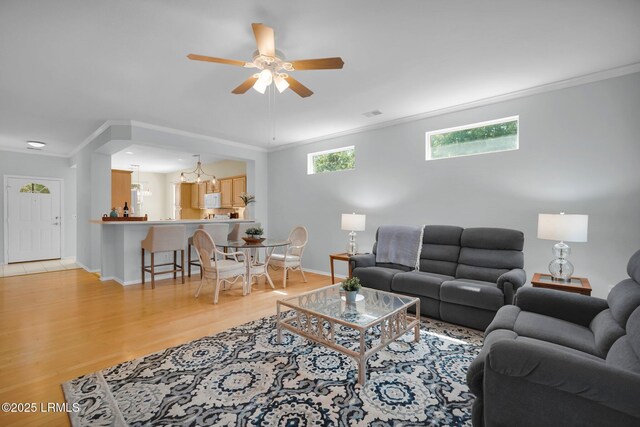 living area featuring ceiling fan with notable chandelier, baseboards, light wood finished floors, and ornamental molding
