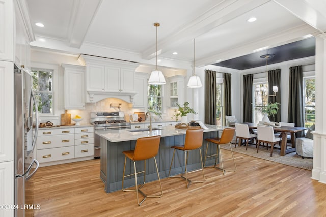 kitchen with an island with sink, sink, white cabinets, stainless steel appliances, and beam ceiling