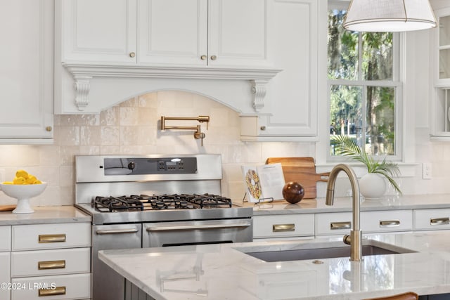 kitchen featuring sink, white cabinetry, light stone countertops, range with two ovens, and backsplash