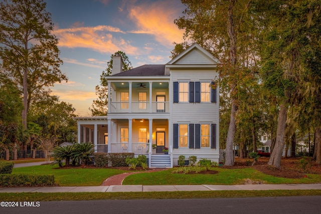 neoclassical home with ceiling fan, a balcony, a yard, and covered porch