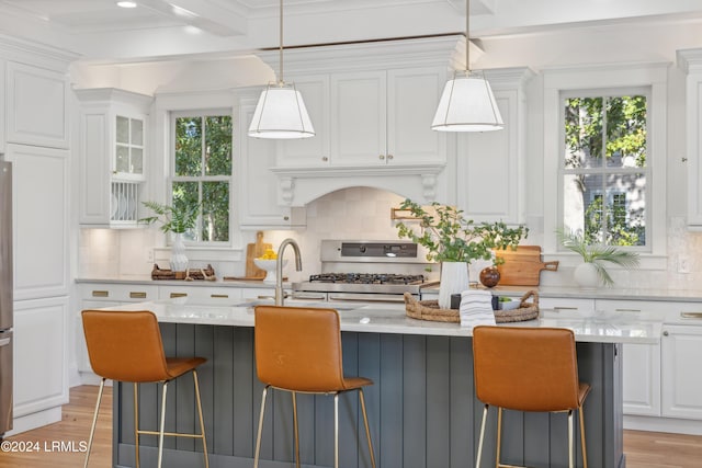 kitchen featuring decorative light fixtures, an island with sink, and white cabinets